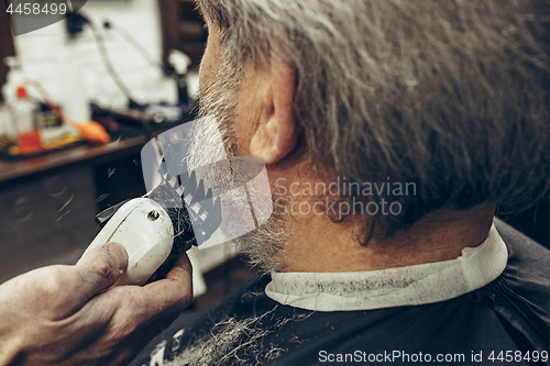 Image of Close-up side back view handsome senior bearded caucasian man getting beard grooming in modern barbershop.