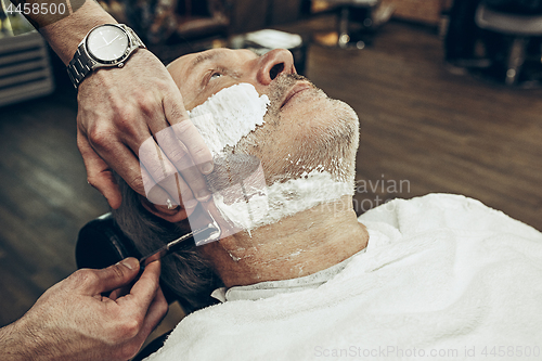 Image of Close-up side top view handsome senior bearded caucasian man getting beard grooming in modern barbershop.