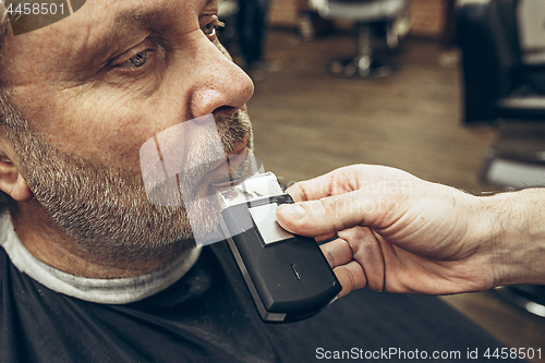 Image of Close-up side view portrait of handsome senior bearded caucasian man getting beard grooming in modern barbershop.