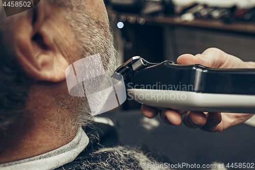 Image of Close-up side back view handsome senior bearded caucasian man getting beard grooming in modern barbershop.