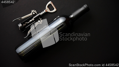 Image of Red wine bottle and corkscrew on black matte background.