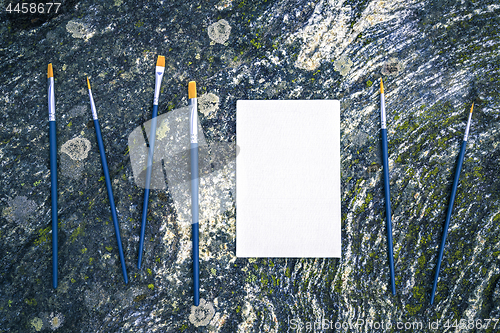 Image of Paintbrushes and blank canvas on mossy stone background