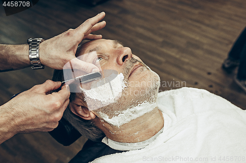 Image of Close-up side top view handsome senior bearded caucasian man getting beard grooming in modern barbershop.