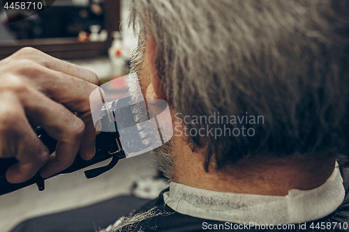 Image of Close-up side back view handsome senior bearded caucasian man getting beard grooming in modern barbershop.