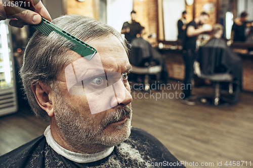 Image of The hands of barber making haircut attractive old man in barbershop