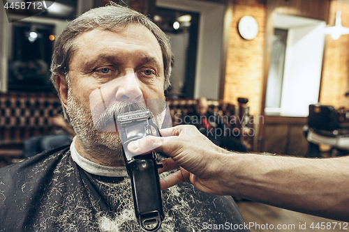 Image of Close-up side view portrait of handsome senior bearded caucasian man getting beard grooming in modern barbershop.