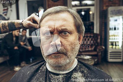 Image of The hands of barber making haircut attractive old man in barbershop