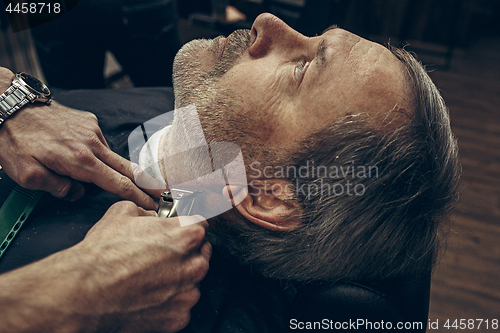 Image of Close-up side back view handsome senior bearded caucasian man getting beard grooming in modern barbershop.