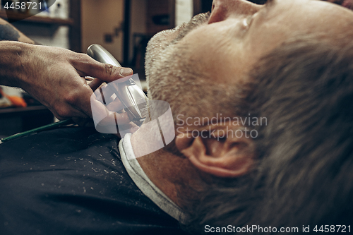 Image of Close-up side back view handsome senior bearded caucasian man getting beard grooming in modern barbershop.