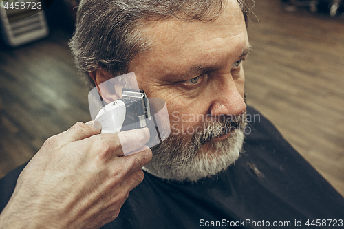 Image of Close-up side view portrait of handsome senior bearded caucasian man getting beard grooming in modern barbershop.