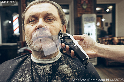 Image of Close-up side view portrait of handsome senior bearded caucasian man getting beard grooming in modern barbershop.