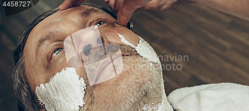 Image of Close-up side top view handsome senior bearded caucasian man getting beard grooming in modern barbershop.