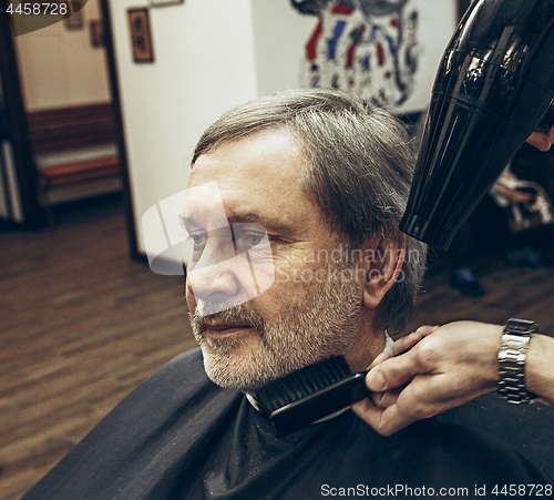 Image of Close-up side view portrait of handsome senior bearded caucasian man getting beard grooming in modern barbershop.