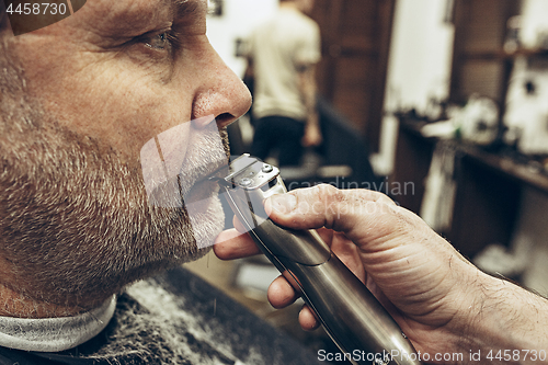 Image of Close-up side profile view portrait of handsome senior bearded caucasian man getting beard grooming in modern barbershop.