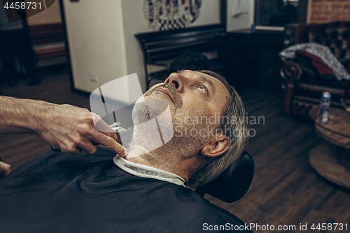 Image of Close-up side profile view portrait of handsome senior bearded caucasian man getting beard grooming in modern barbershop.