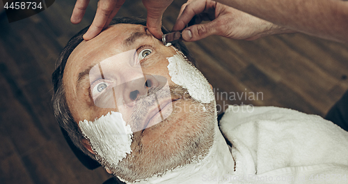 Image of Close-up side top view handsome senior bearded caucasian man getting beard grooming in modern barbershop.