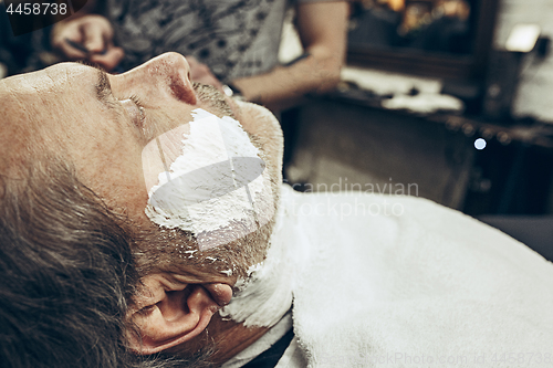 Image of Close-up side view portrait of handsome senior bearded caucasian man getting beard grooming in modern barbershop.