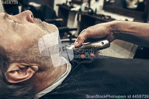 Image of Close-up side profile view portrait of handsome senior bearded caucasian man getting beard grooming in modern barbershop.