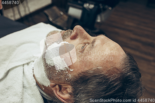 Image of Close-up side top view handsome senior bearded caucasian man getting beard grooming in modern barbershop.