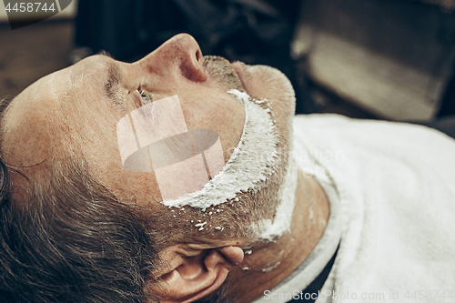 Image of Close-up side top view handsome senior bearded caucasian man getting beard grooming in modern barbershop.