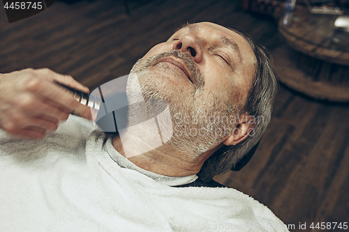 Image of Close-up side top view handsome senior bearded caucasian man getting beard grooming in modern barbershop.