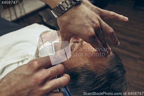 Image of Close-up side top view handsome senior bearded caucasian man getting beard grooming in modern barbershop.