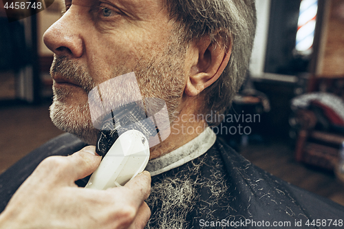 Image of Close-up side view portrait of handsome senior bearded caucasian man getting beard grooming in modern barbershop.