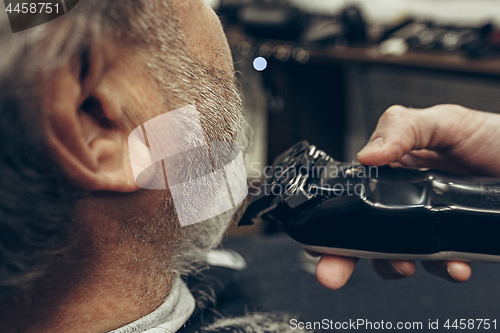 Image of Close-up side back view handsome senior bearded caucasian man getting beard grooming in modern barbershop.