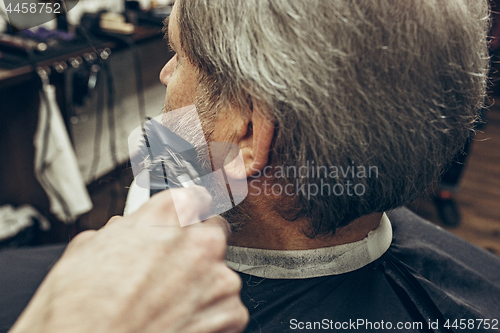 Image of Close-up side back view handsome senior bearded caucasian man getting beard grooming in modern barbershop.