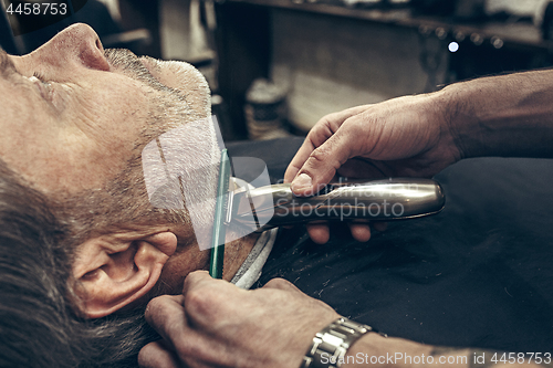 Image of Close-up side profile view portrait of handsome senior bearded caucasian man getting beard grooming in modern barbershop.