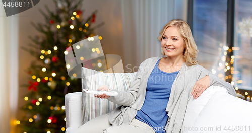 Image of smiling woman with tv remote at home on christmas