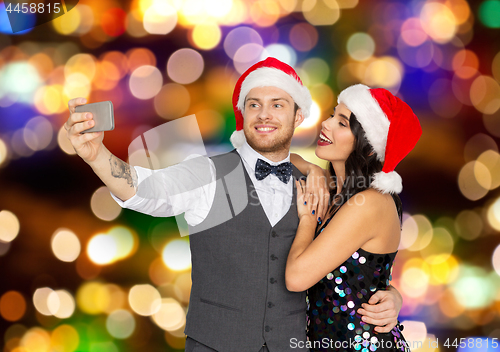 Image of couple in santa hats taking selfie at christmas