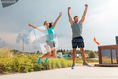 Image of happy couple in sports clothes jumping on beach