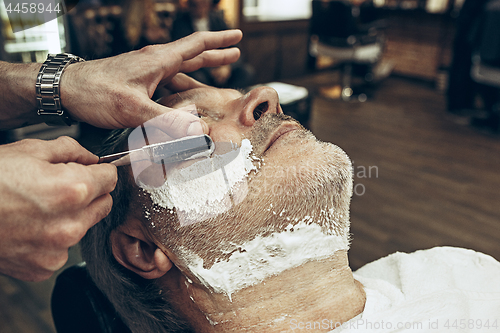 Image of Close-up side top view handsome senior bearded caucasian man getting beard grooming in modern barbershop.