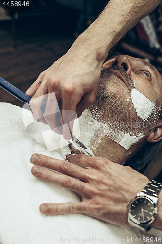 Image of Close-up side top view handsome senior bearded caucasian man getting beard grooming in modern barbershop.