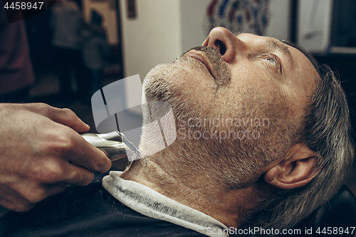 Image of Close-up side profile view portrait of handsome senior bearded caucasian man getting beard grooming in modern barbershop.