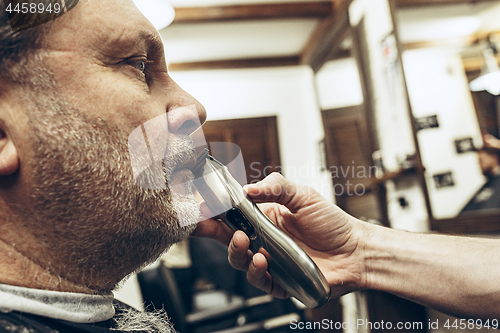 Image of Close-up side profile view portrait of handsome senior bearded caucasian man getting beard grooming in modern barbershop.