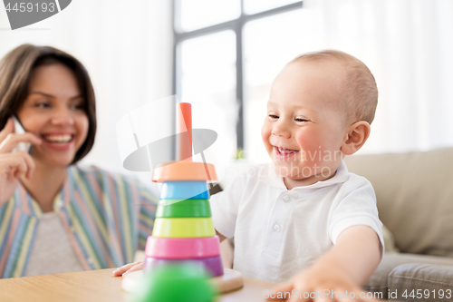 Image of baby playing toy and mother calling on smartphone