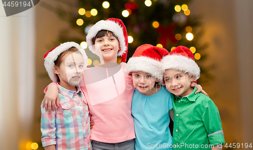 Image of happy children in santa hats hugging on christmas