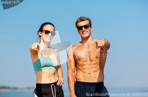 Image of happy couple in sports clothes and shades on beach