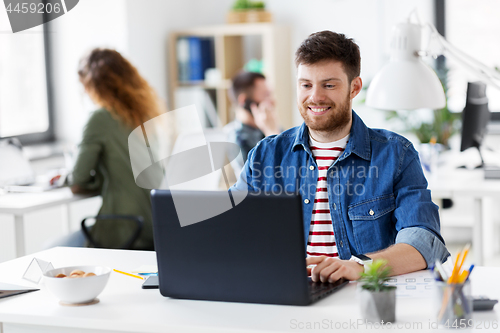 Image of smiling creative man with laptop working at office