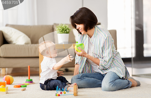 Image of happy mother giving sippy cup to baby son at home