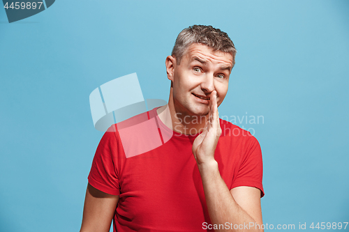 Image of The young man whispering a secret behind her hand over blue background