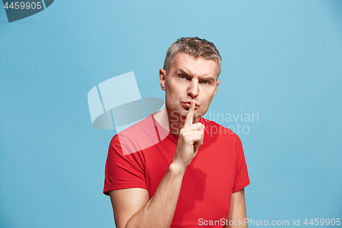 Image of The young man whispering a secret behind her hand over blue background