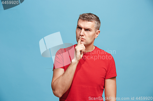 Image of The young man whispering a secret behind her hand over blue background