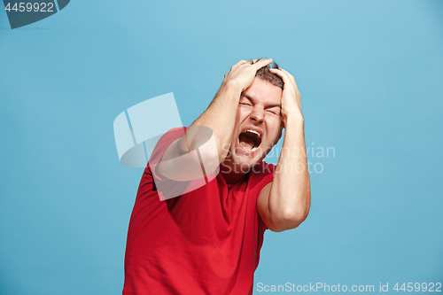 Image of The young emotional angry man screaming on blue studio background