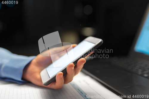 Image of close up of hand with smartphone at night office