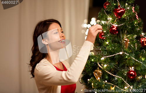 Image of happy woman decorating christmas tree at home