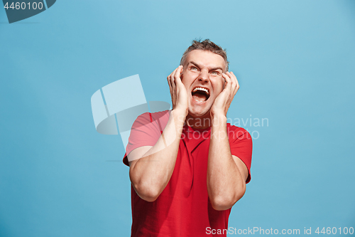 Image of The young emotional angry man screaming on blue studio background