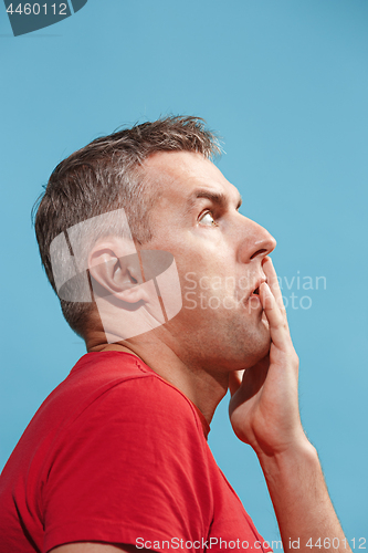 Image of Suspiciont. Doubtful pensive man with thoughtful expression making choice against blue background